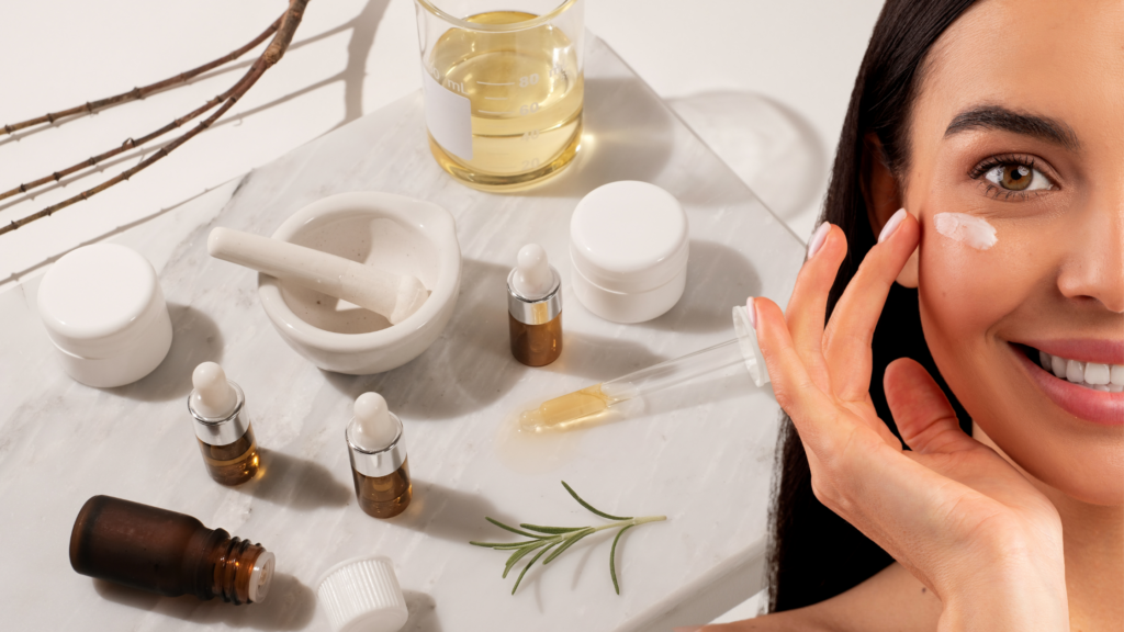 A smiling woman applying cream to her face beside a collection of skincare products, including amber dropper bottles, white jars, a mortar and pestle, a glass beaker with oil, and rosemary sprigs on a marble surface.